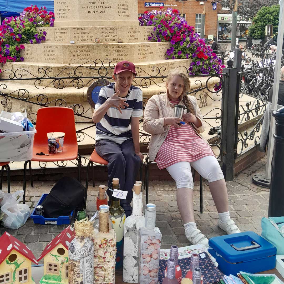 Two people sat on chairs behind a table at a market stall