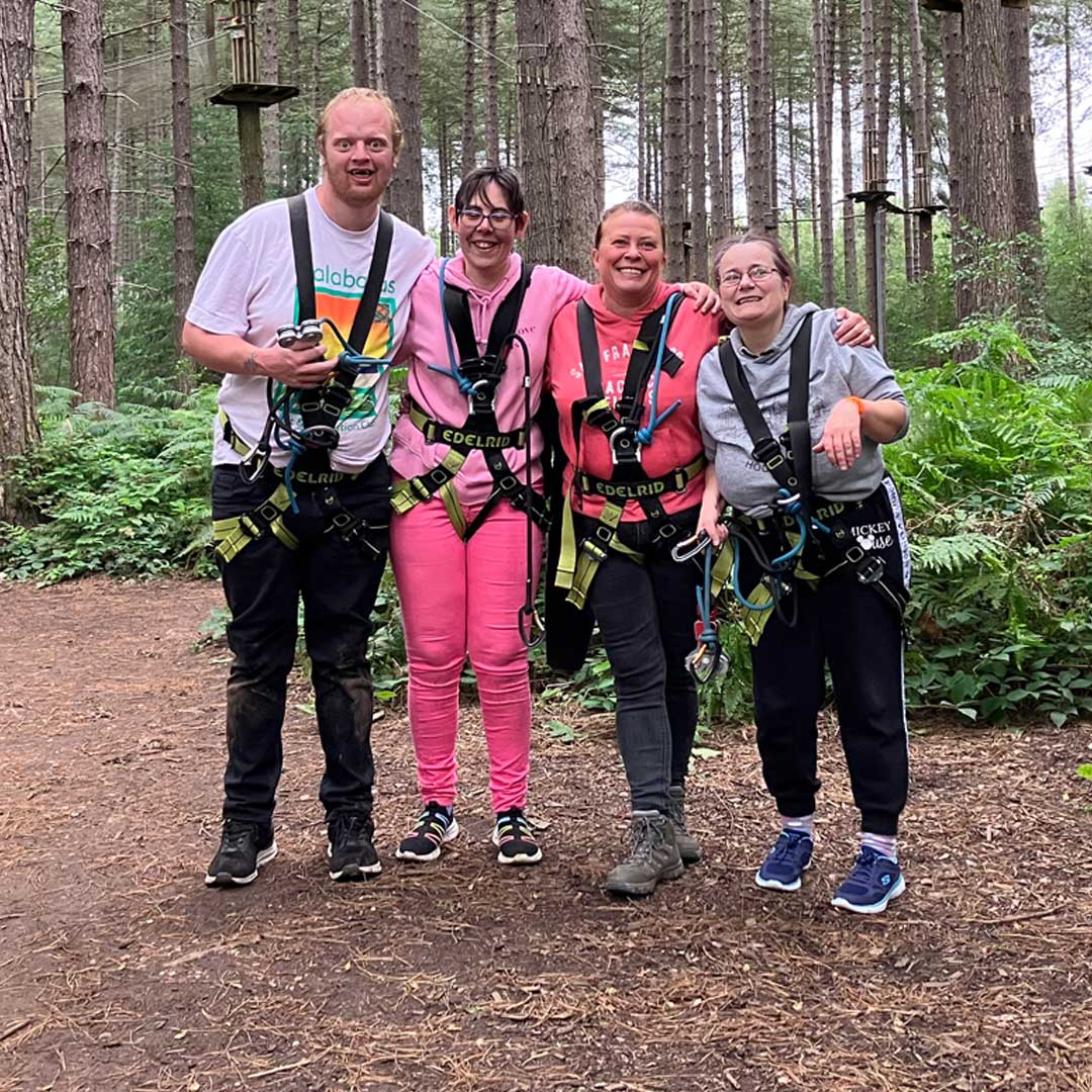 Four people stood next to a Go Ape course wearing harnesses