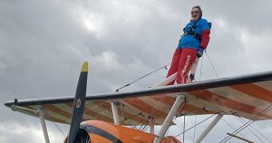 Lady in red jumpsuit stood on top of an orange biplane about to do a wing walk