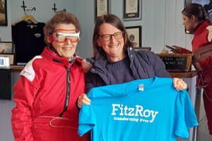 Lady in red jumpsuit stood next to lady holding up bright blue FitzRoy T-shirt