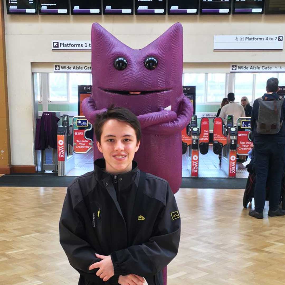 Person in dark jacket stood in front of purple statue at train station