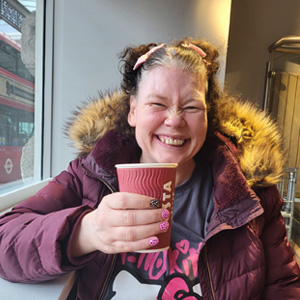 Woman in magenta coat holding up a Costa coffee cup
