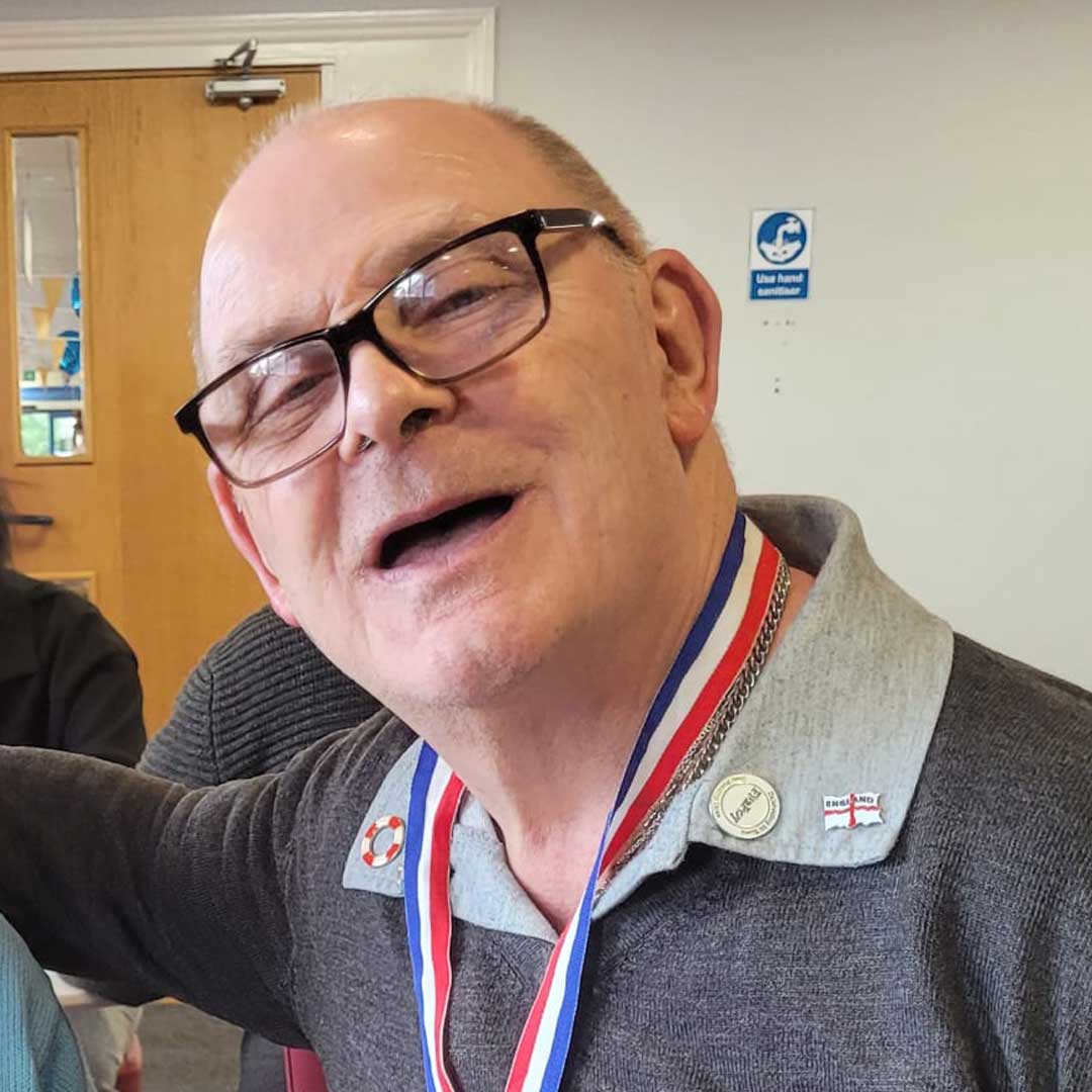 Man wearing glasses and a grey jumper, with a medal hanging around his neck