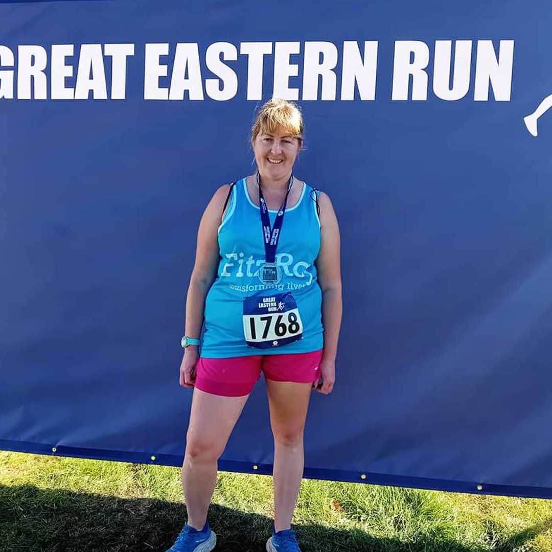 Woman wearing bright blue running vest and pink shorts stood in front of a banner saying Great Eastern Run