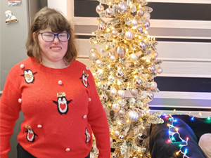 Woman wearing red jumper with penguins on stood next to a Christmas tree