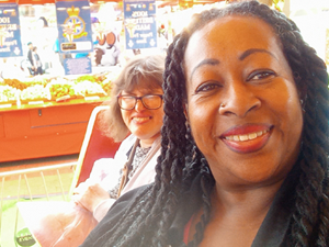 Two women smile for the camera, with a market stall behind them