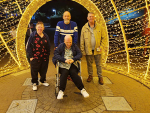 Man in wheelchair surrounded by friends in a tunnel of fairy lights