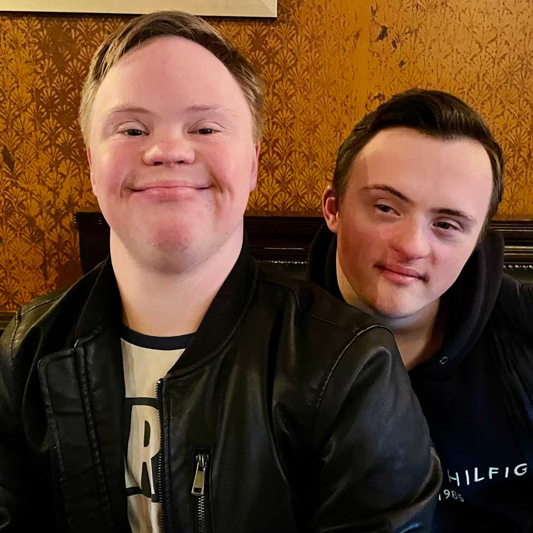 Two young men smile for the camera sat on a bench in a pub