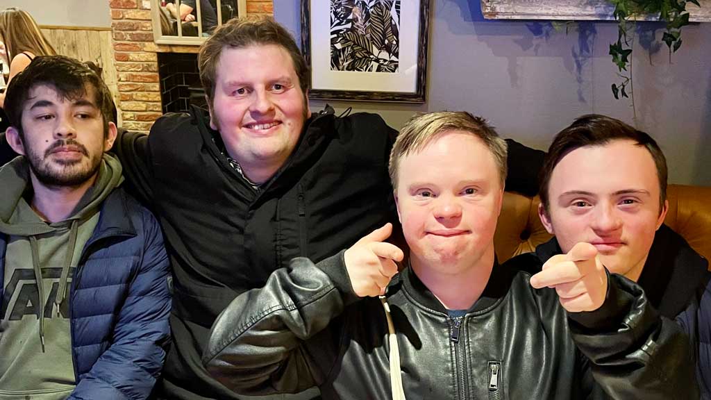 Four young men with learning disabilities sat on a bench in a pub smile for the camera