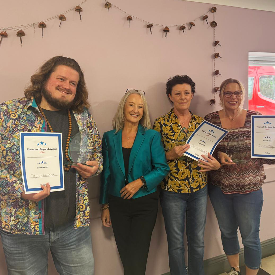 Four people smile for the camera, with three holding awards certificates