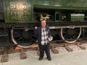 Man in checked shirt and coat stood in front of a green train