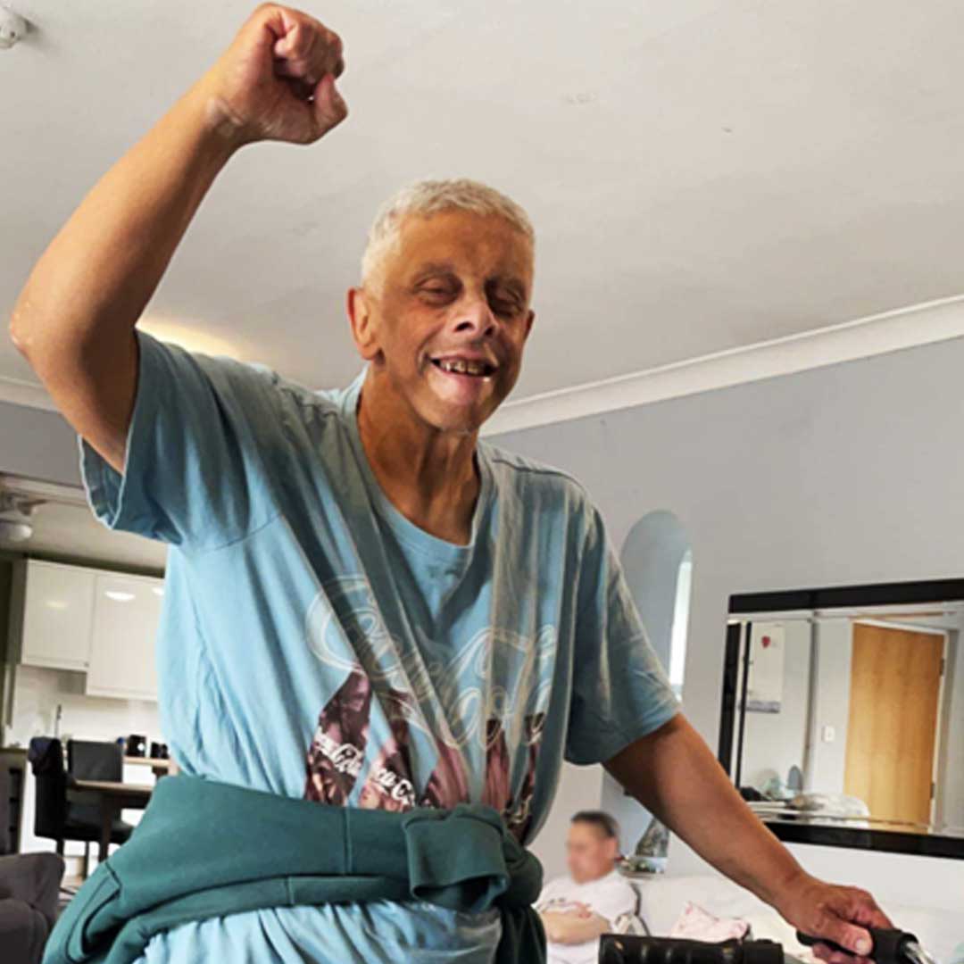 Man wearing pale blue T-shirt with a jumper tied round his waist punches the air with one hand