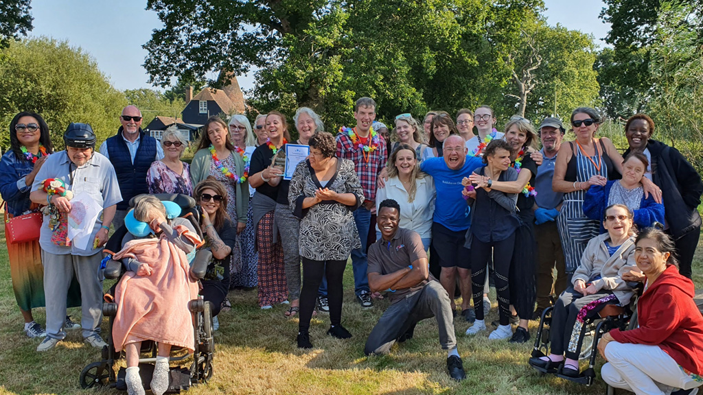 A big group of people smile for the camera outdoors on a sunny day