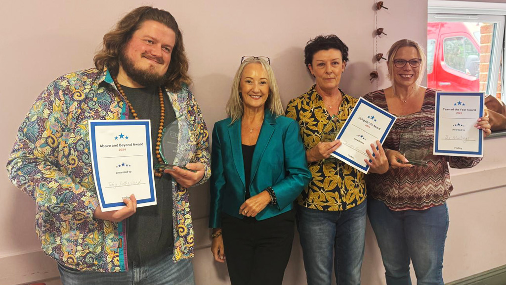 Four people smile for the camera with three holding up certificates