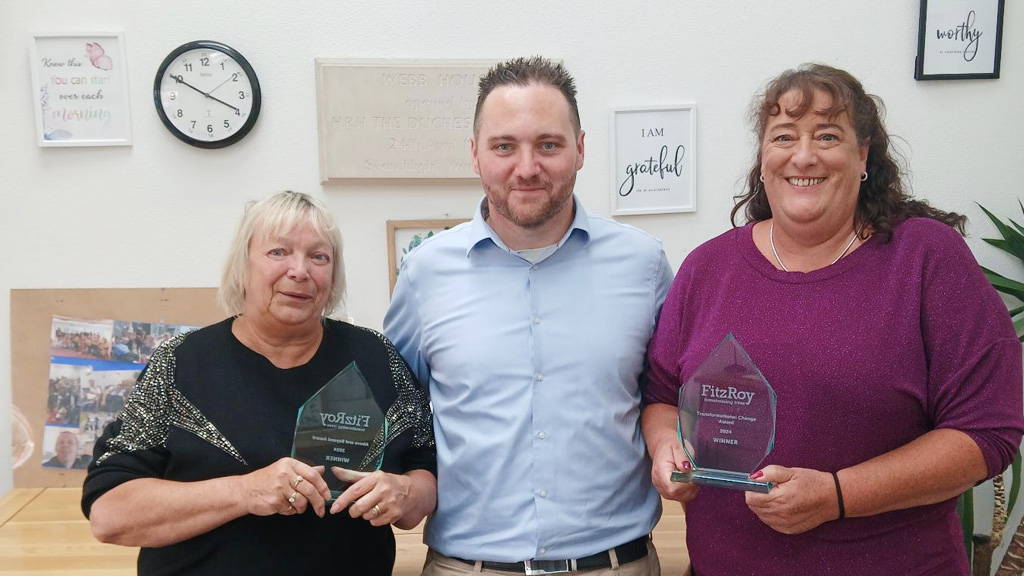 Three people smile for the camera, with two holding glass trophies