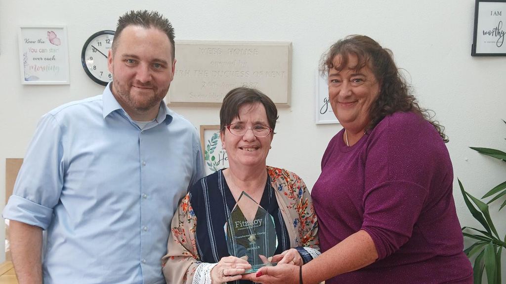 Three people smile for the camera, with the person in the middle being handed an award