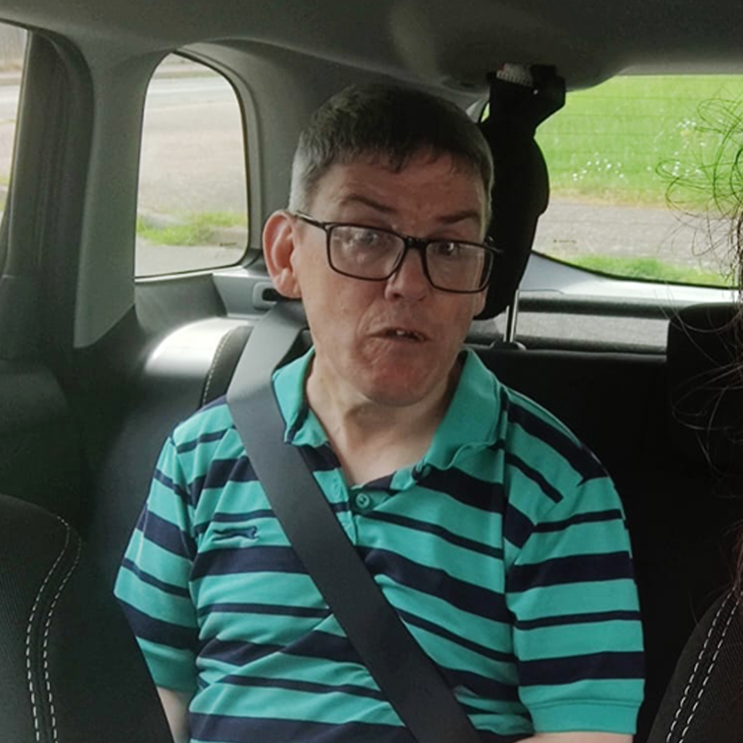 Man in striped green shirt sat in back seat of car with a seat belt on