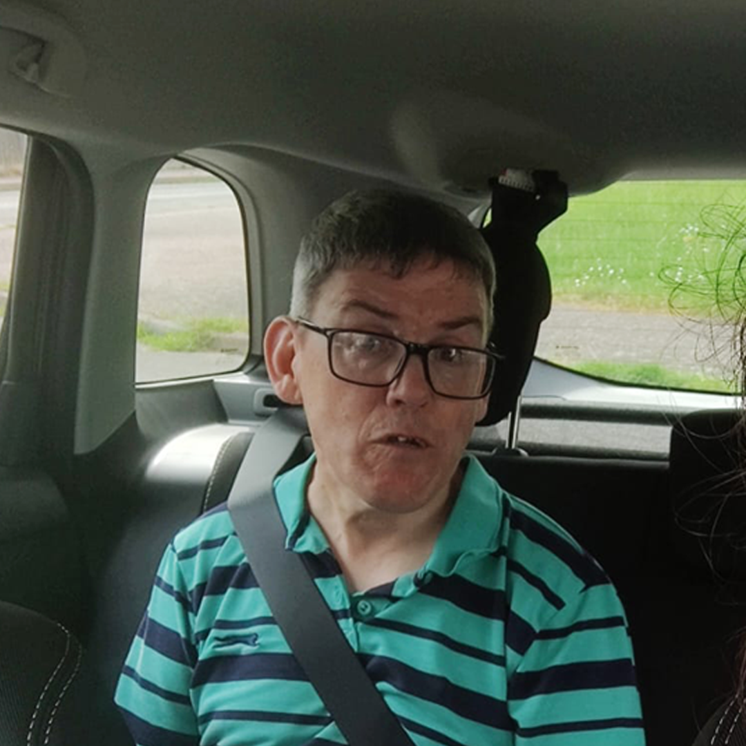 Man in striped green shirt sat in back seat of car with a seat belt on