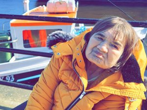 Woman wearing orange coat sat in a wheelchair in front of railings on a seafront