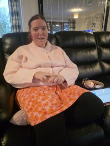 Libby is sitting on the sofa making a sign with her hands