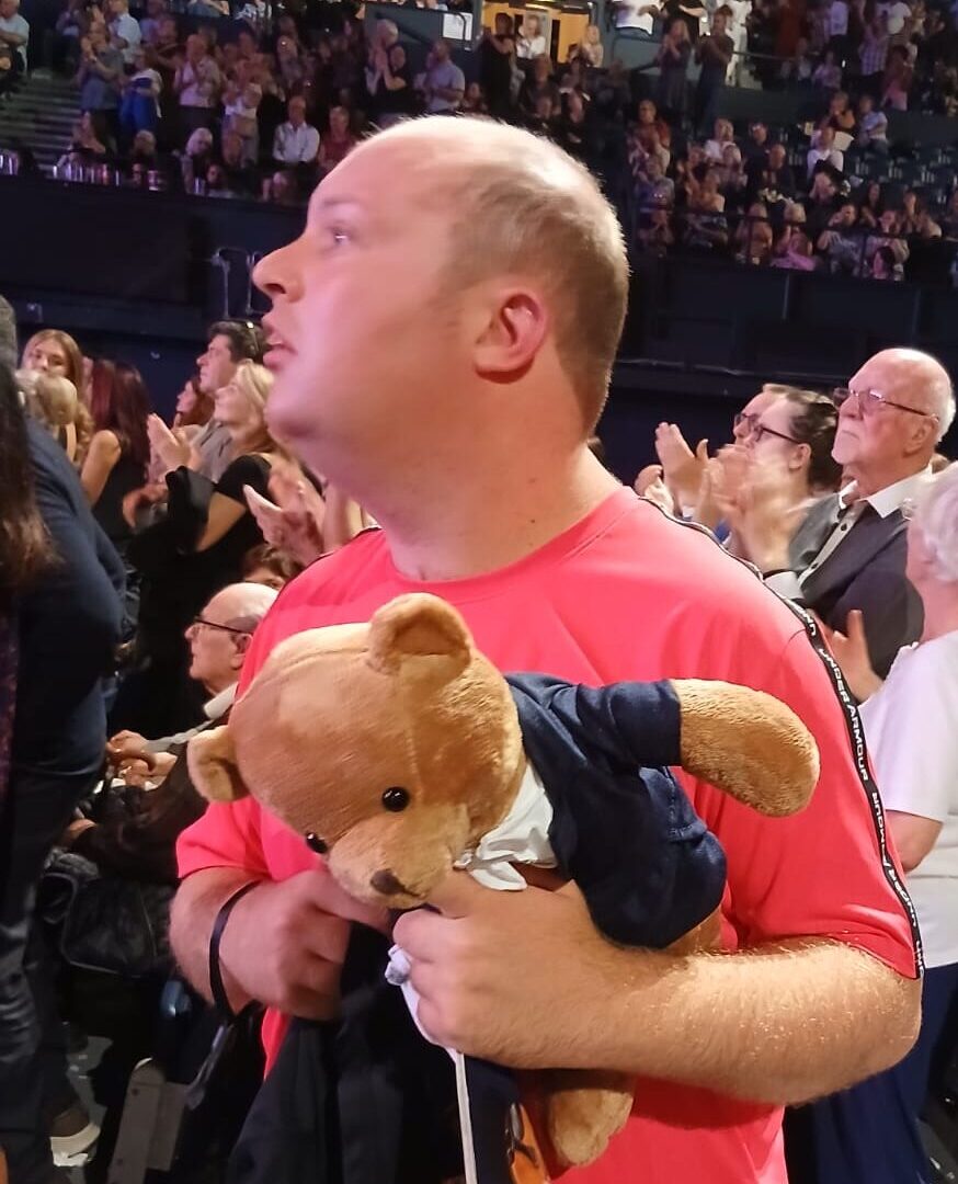 Carl is standing in the crowd at Wembley, carrying his Andre Rieu merch and looking at the stage